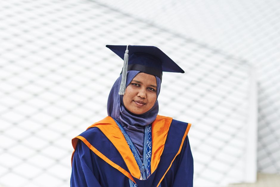 Muslim woman in graduation attire poses confidently outdoors in Malaysia.